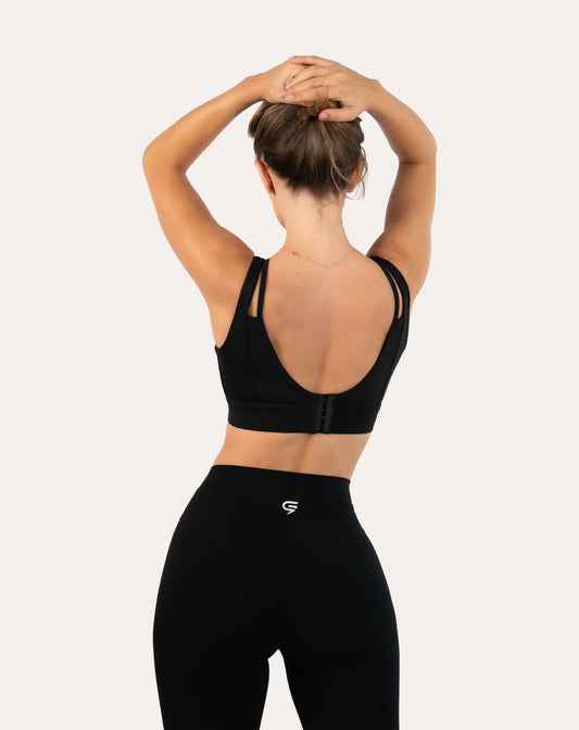Back view with arms raised of black high support sports bra showing deep U and hook-and-eye closure