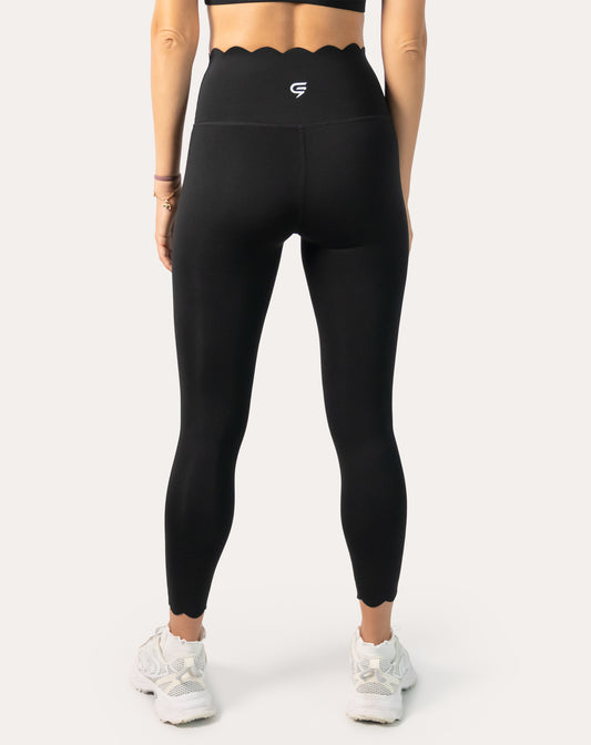 Back view of women’s black gym leggings featuring a scallop high waist and scalloped ankle hems with squat-proof coverage