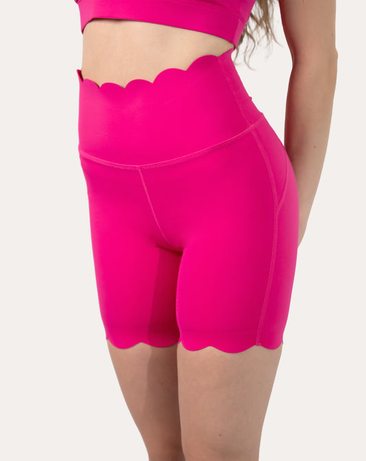 Front left three-quarter close-up of hot pink yoga shorts showing scalloped high waist and hem