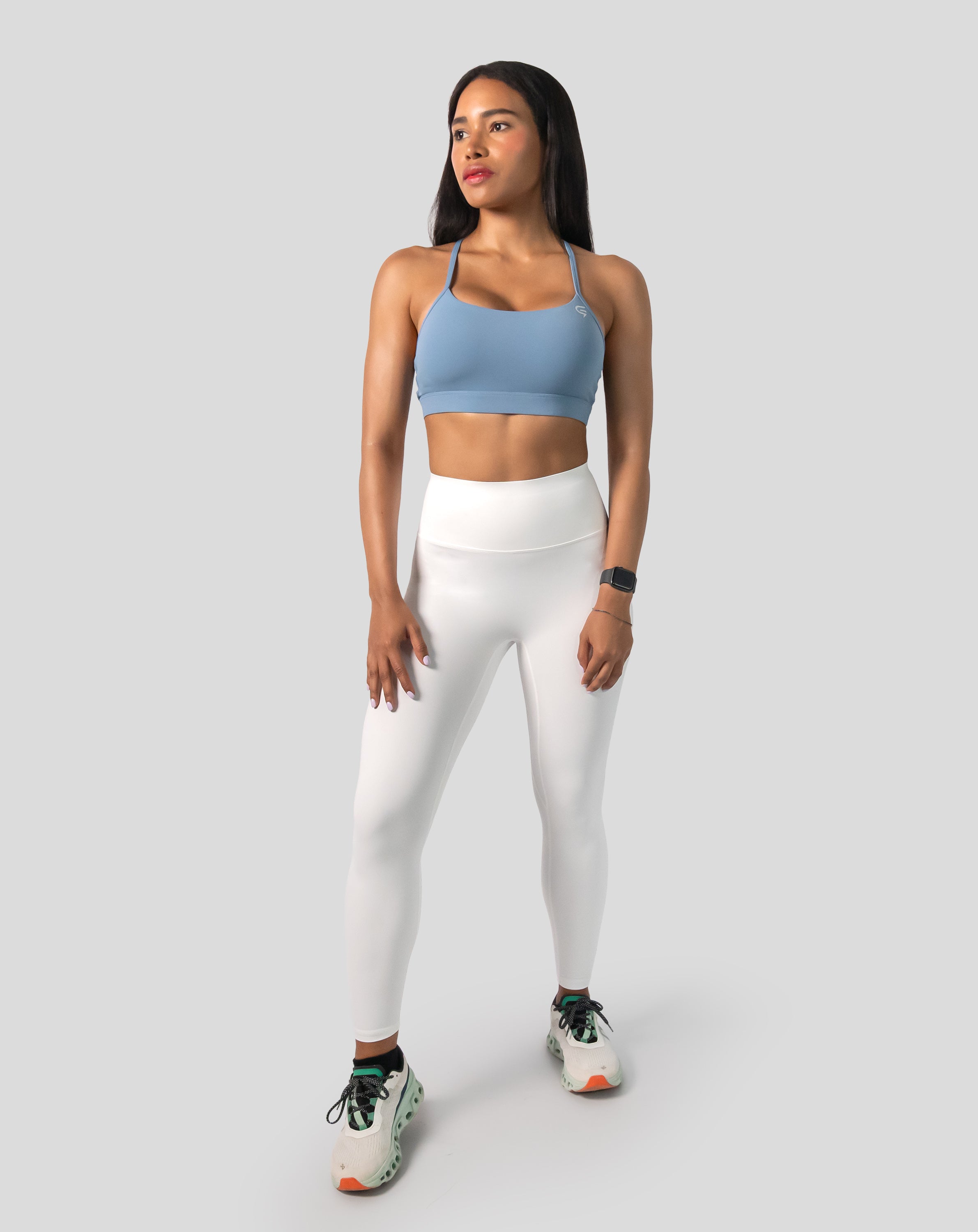 Full-body front view wearing a light blue strappy sports bra paired with white leggings
