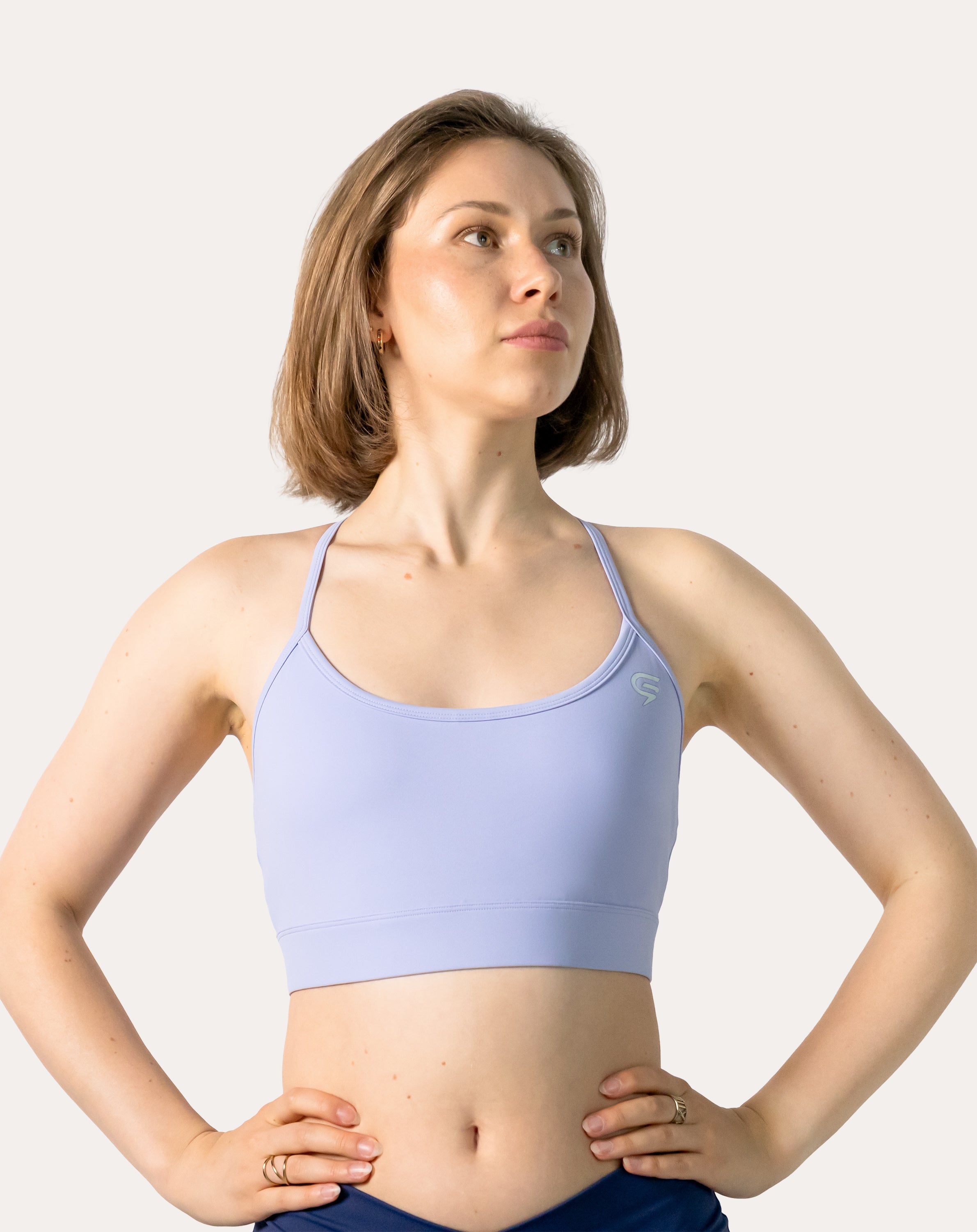 Mid-length front of lilac racerback sports bra with hands on hips; scoop neck and wide band