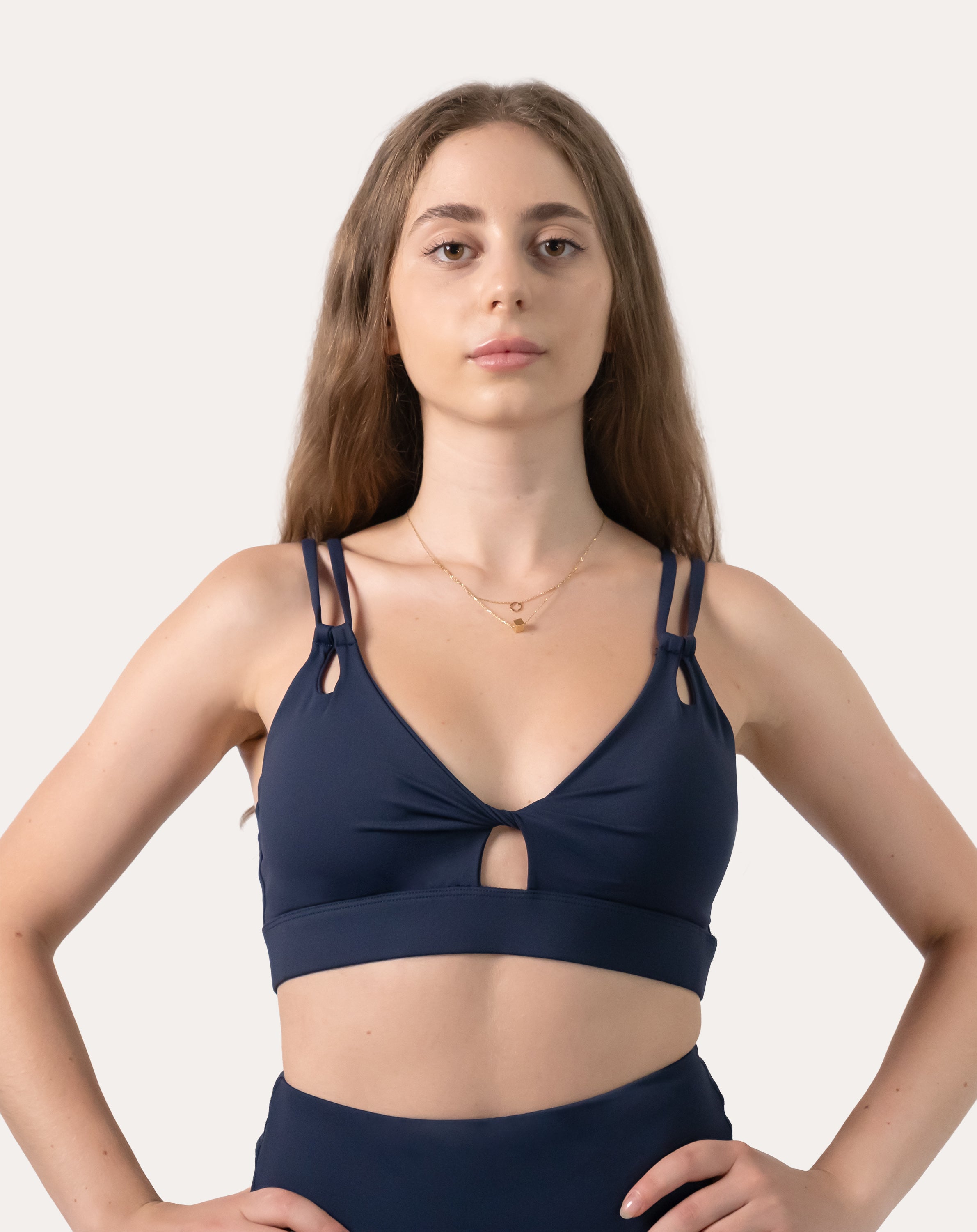 Navy sports bra front mid-length with hands on hips; V-neck and double straps shown
