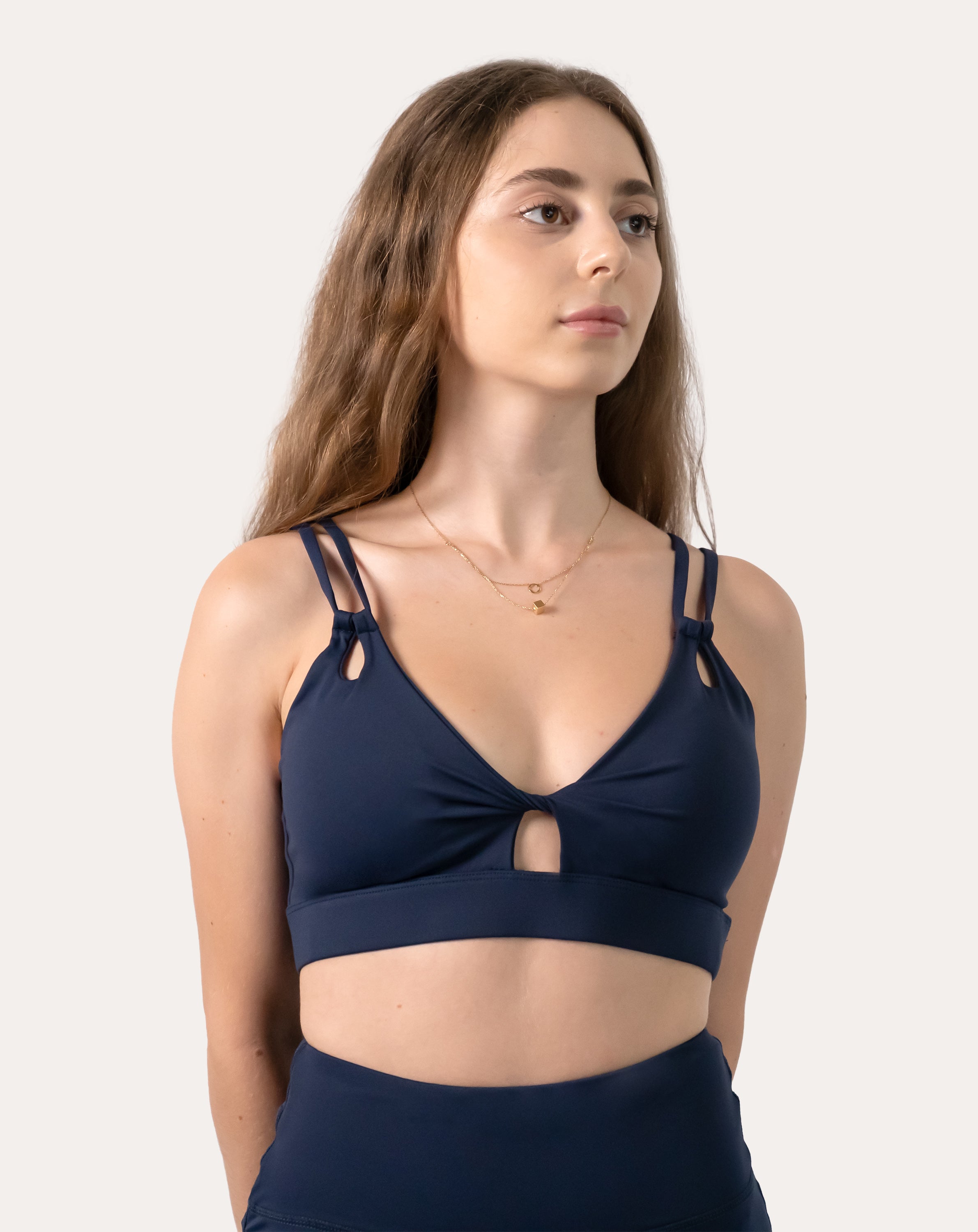 Navy sports bra three-quarter front with hands on hips; V-neck and supportive band visible