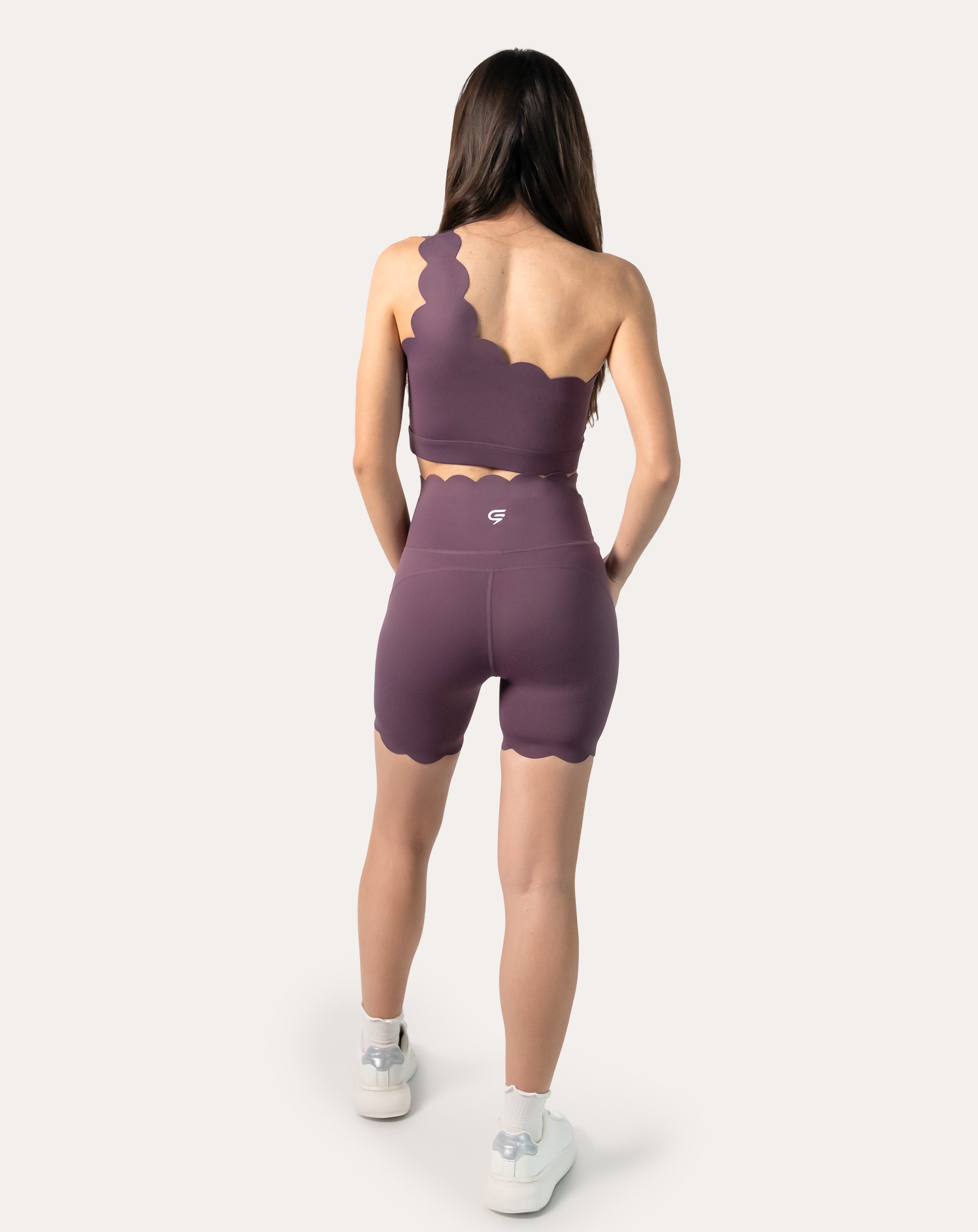 Back view of the plum one-shoulder gym set highlighting scallop edges and wide waistband