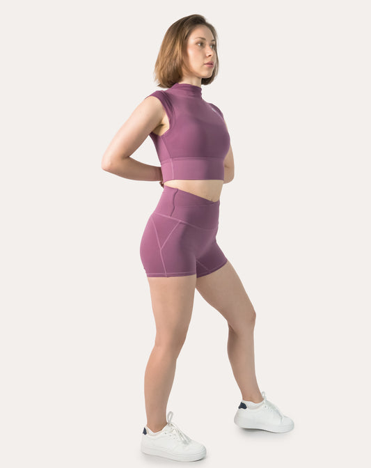 3/4 side view showing profile of plum gym shorts set; high-neck crop and V-waist shorts.
