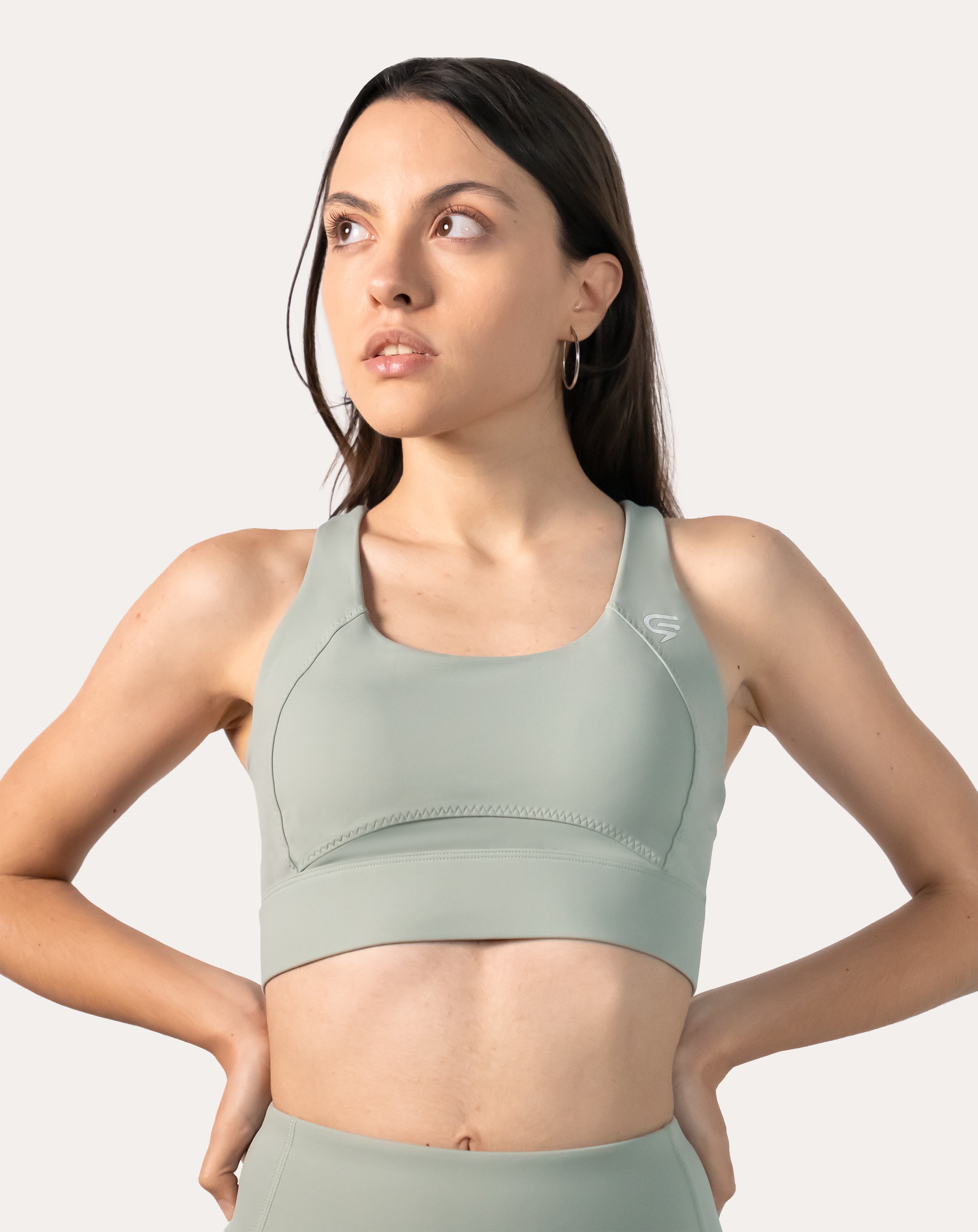 Three-quarter front view of the sage green running sports bra with hands on hips