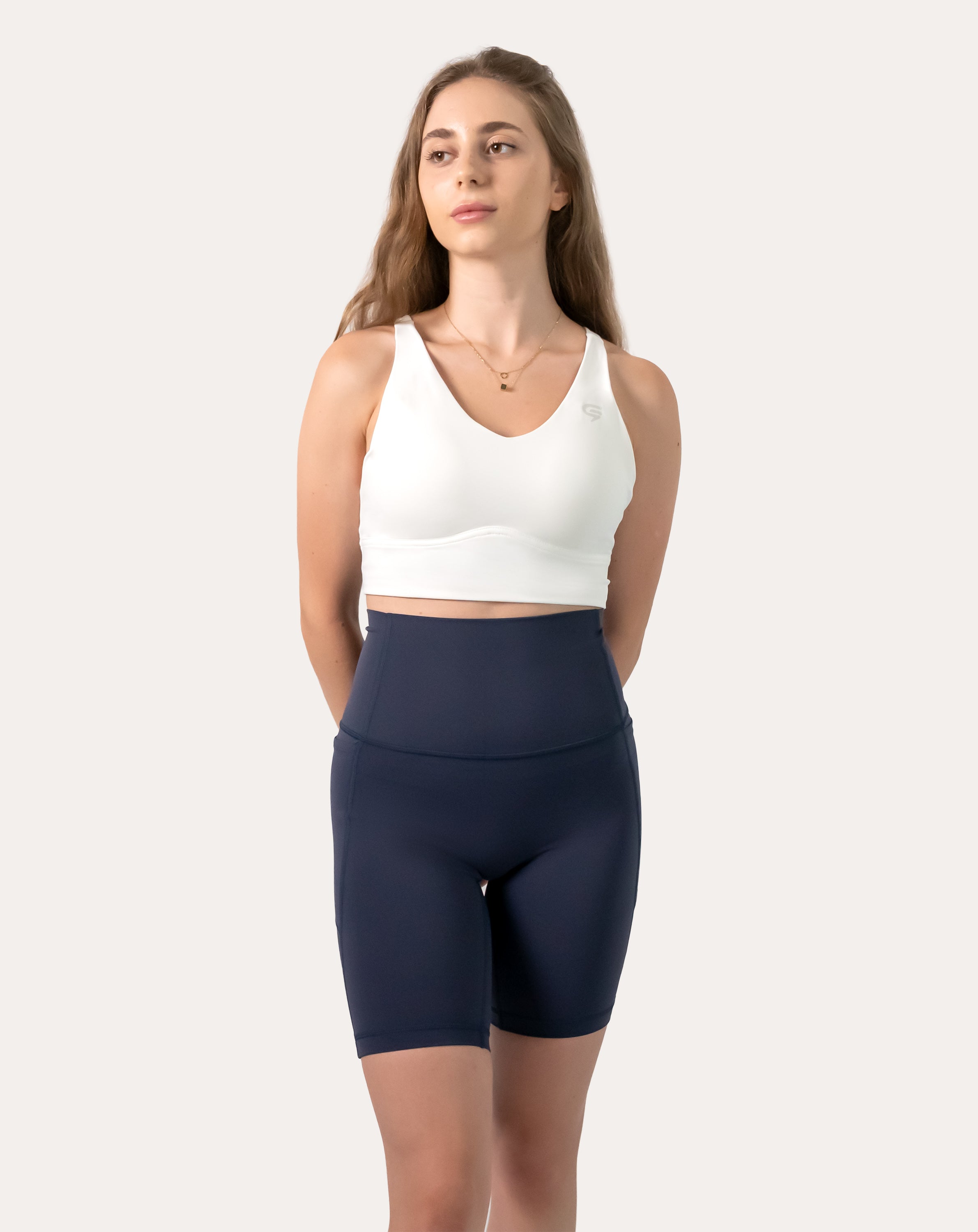 Full-length front view of white backless sports bra with smooth V-neck and longline underband