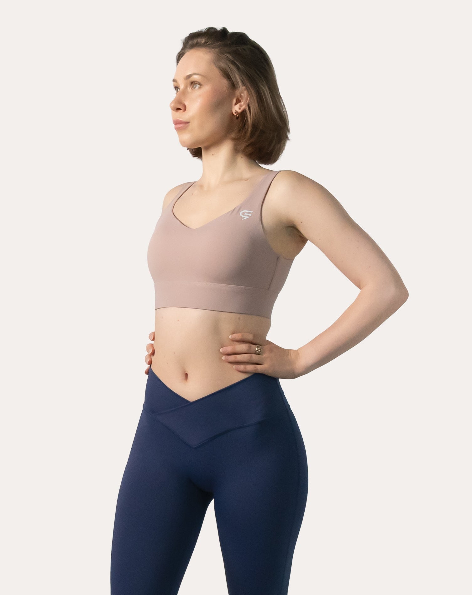 Front view of baby pink sports bra with hands on hips; smooth wireless front and wide straps