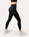Angled back view highlighting contour seams and a scallop waistband on high-waist black leggings during a stretch stance
