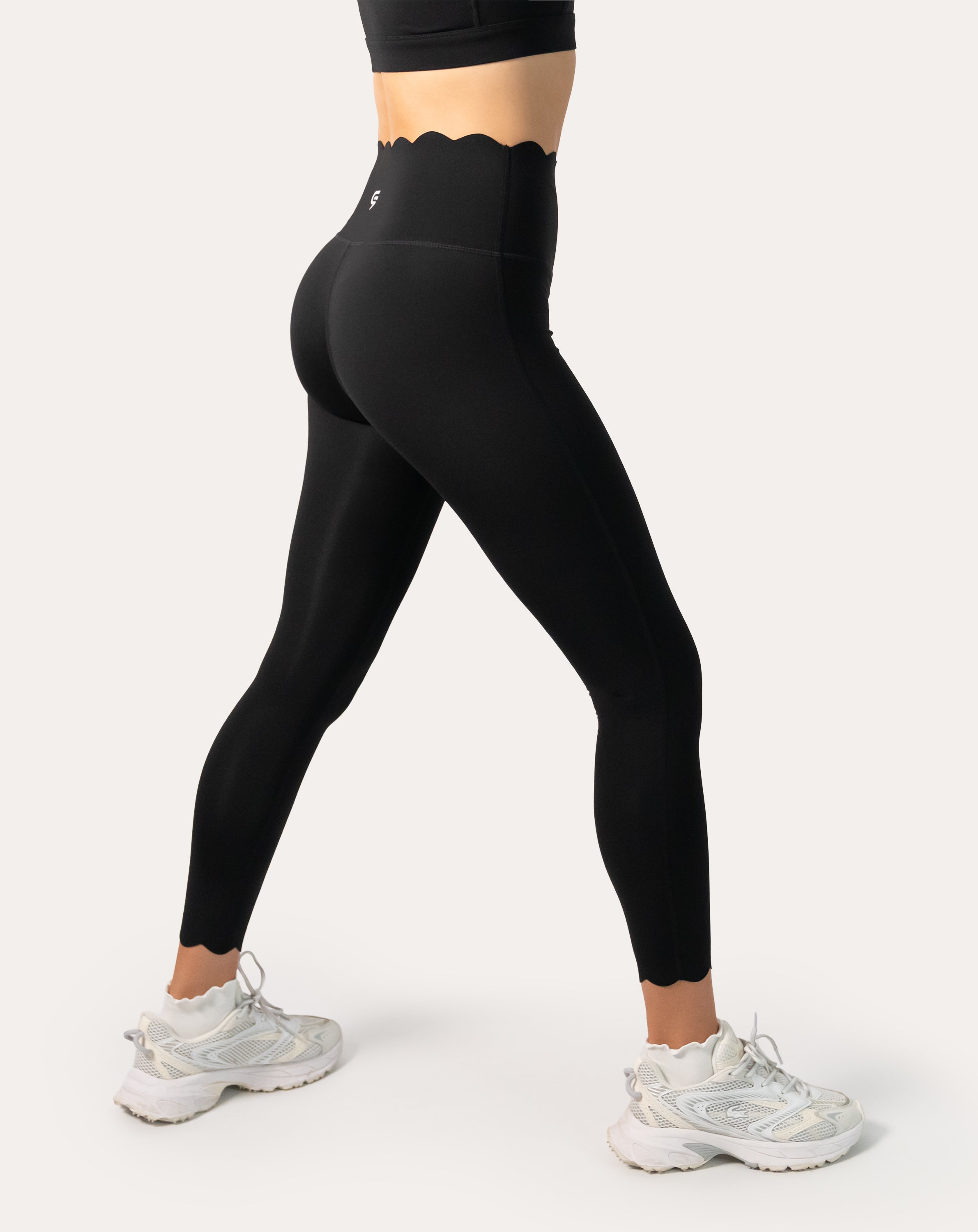 Angled back view highlighting contour seams and a scallop waistband on high-waist black leggings during a stretch stance