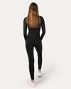 Back view, mid distance, of black long-sleeve women’s jumpsuit with clean lines