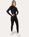 Front full-body view of black long-sleeve women’s jumpsuit, hands on hips