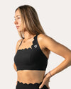 Front three-quarter view of black padded sports bra with scalloped neckline and wide underband