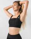 Front view with arms raised of black running sports bra featuring a square neck and wide straps