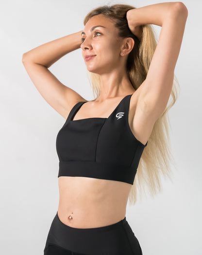 Front view with arms raised of black running sports bra featuring a square neck and wide straps
