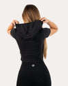 Back view of black short sleeve gym top for women with hood lifted to show wrap hood
