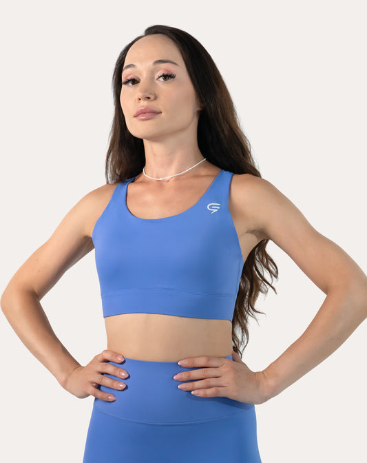 Front close-up of blue sports bra with scoop neck and wide underband; hands on hips
