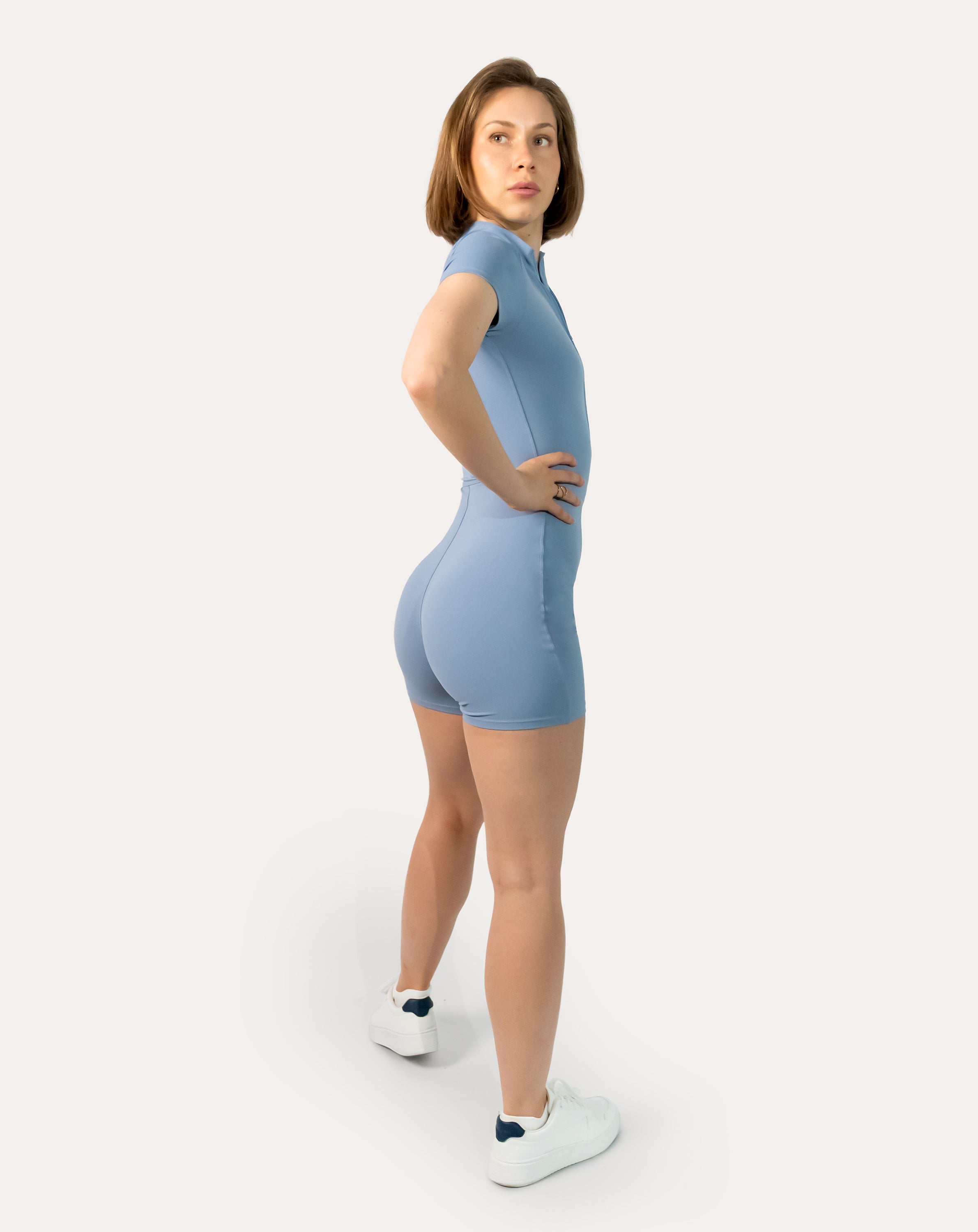 Blue sports jumpsuit with short sleeves; back right three quarter view, hands on hips