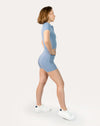 Blue sports jumpsuit with short sleeves; right three quarter view in a step stance.