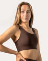 Close-up front angle of a woman wearing a brown high-support sports bra with scoop neckline, wide straps, and smooth underband.
