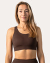 Frontal portrait of model in a brown sports bra featuring a scoop front, supportive wide underband, and lightly padded cups.