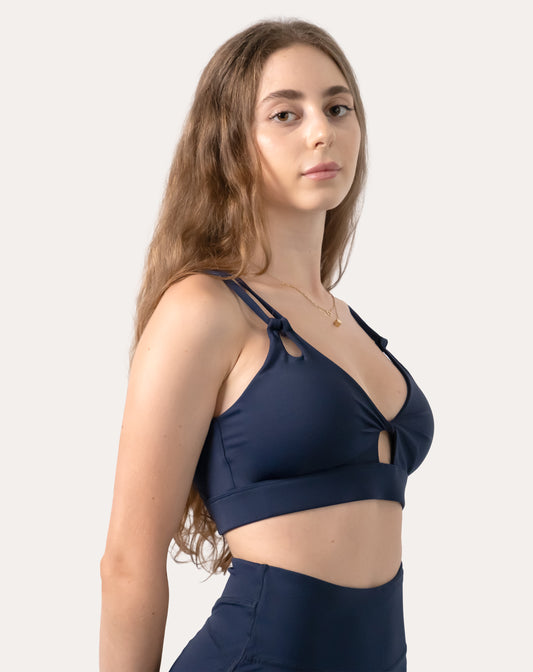 Navy sports bra, three-quarter front close-up showing V-neck with subtle keyhole and double straps