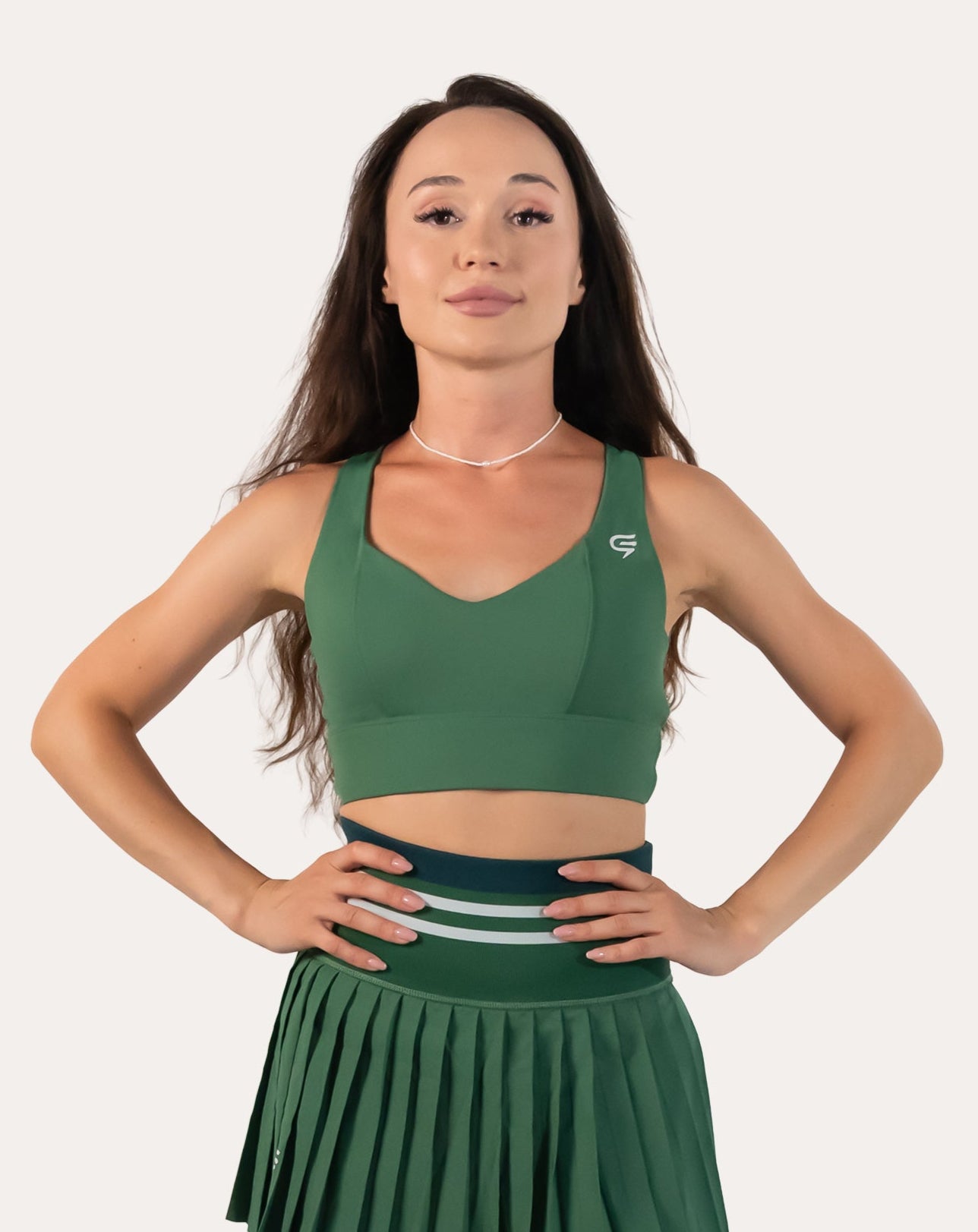 Front view of the forest green longline sports bra with hands on hips; V-neck and supportive band
