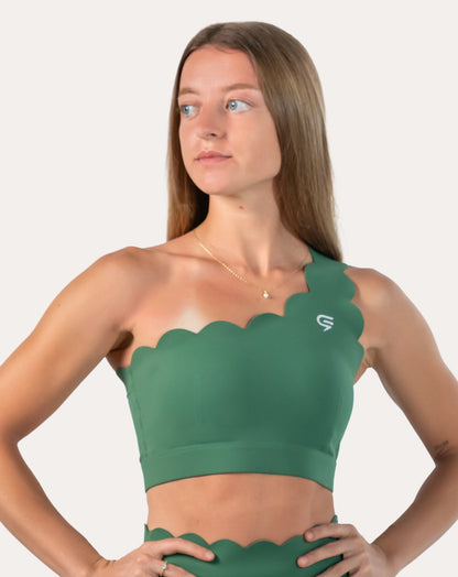 Front three-quarter view of green sports bra with scalloped one-shoulder neckline and wide underband