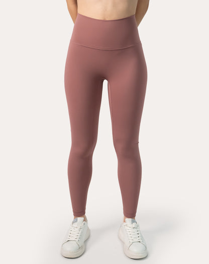Front view of women’s high-waisted leggings in rose-clay pink; buttery-soft, ankle-length fit styled with white sneakers