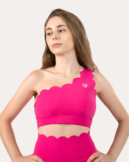 Front three-quarter view of hot pink sports bra with one-shoulder scalloped strap and wide underband