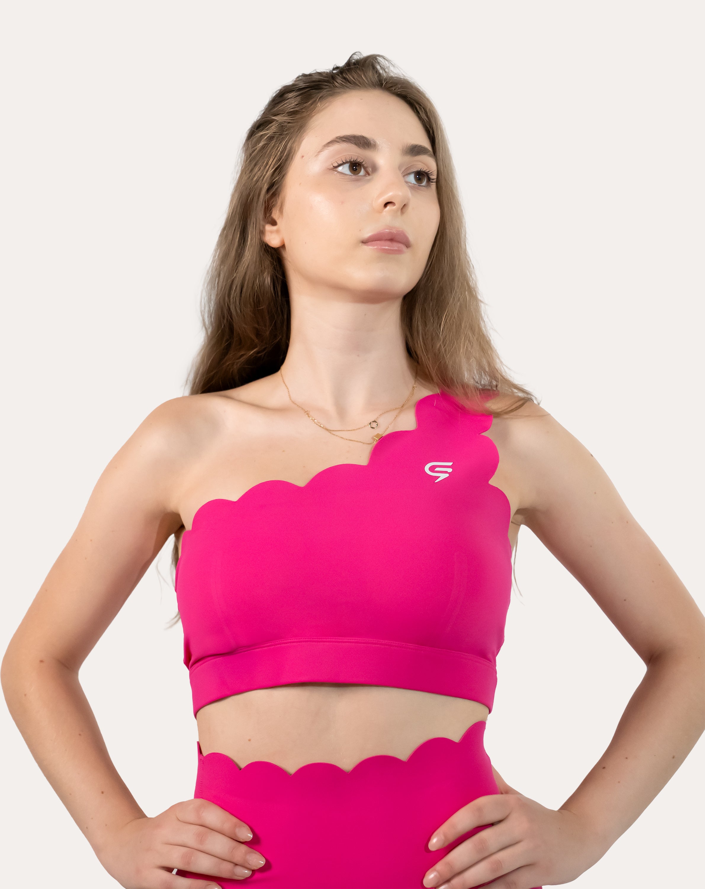 Front view of hot pink sports bra with scalloped one-shoulder strap and wide underband