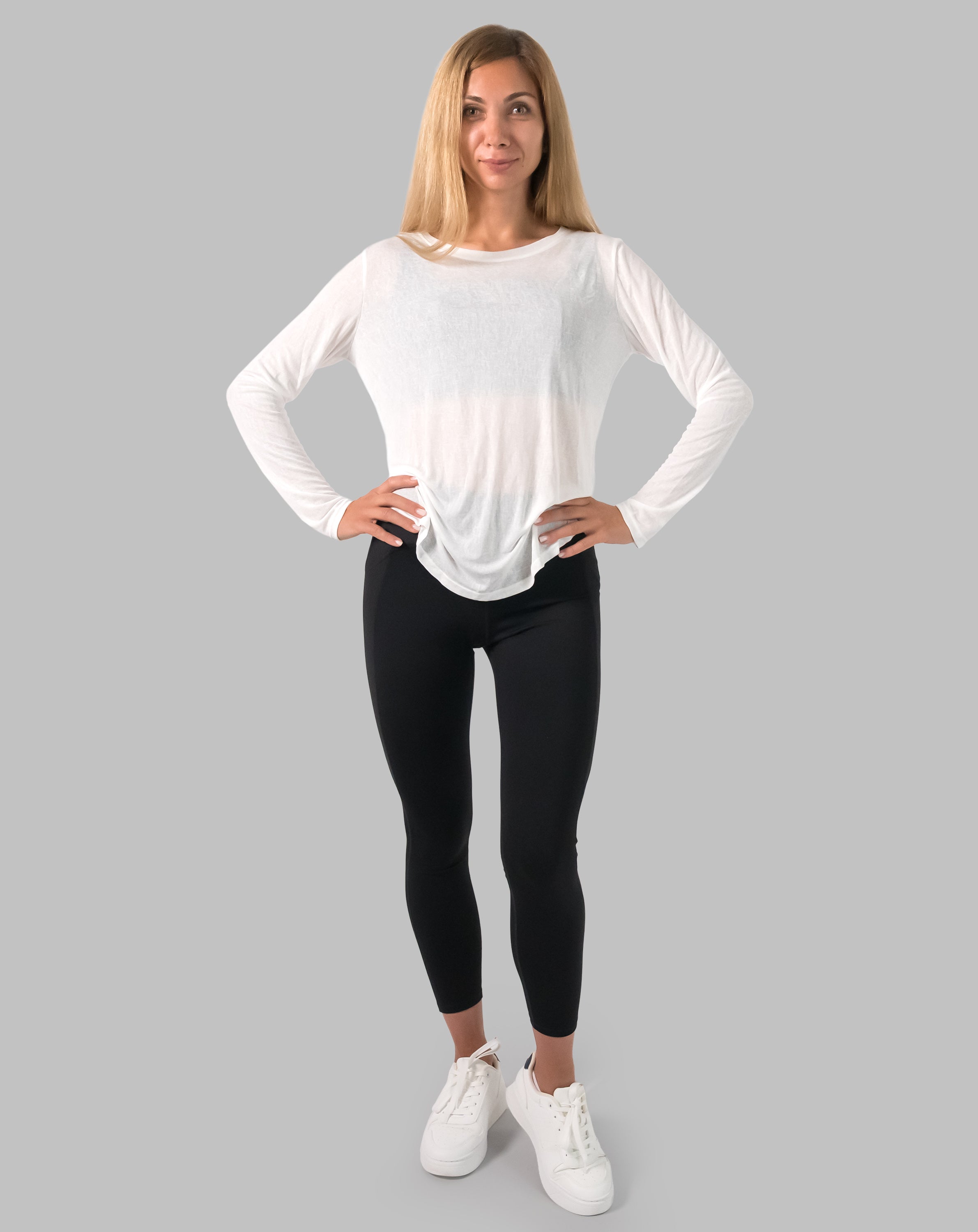 Front full-length, hands on hips; white ladies long sleeve gym top with breathable sheer knit