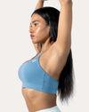 Front three-quarter view of light blue strappy sports bra, arm raised to show scoop neck and light padding