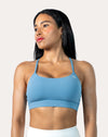 Front three-quarter view of light blue strappy sports bra with scoop neckline and thin straps