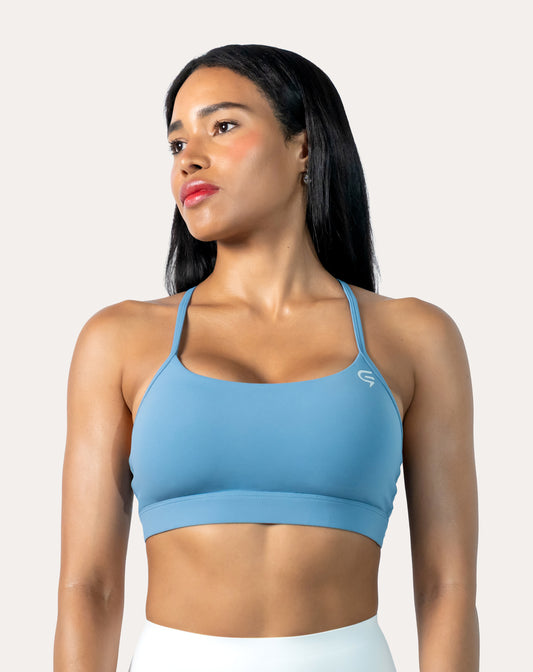 Front three-quarter view of light blue strappy sports bra with scoop neckline and thin straps