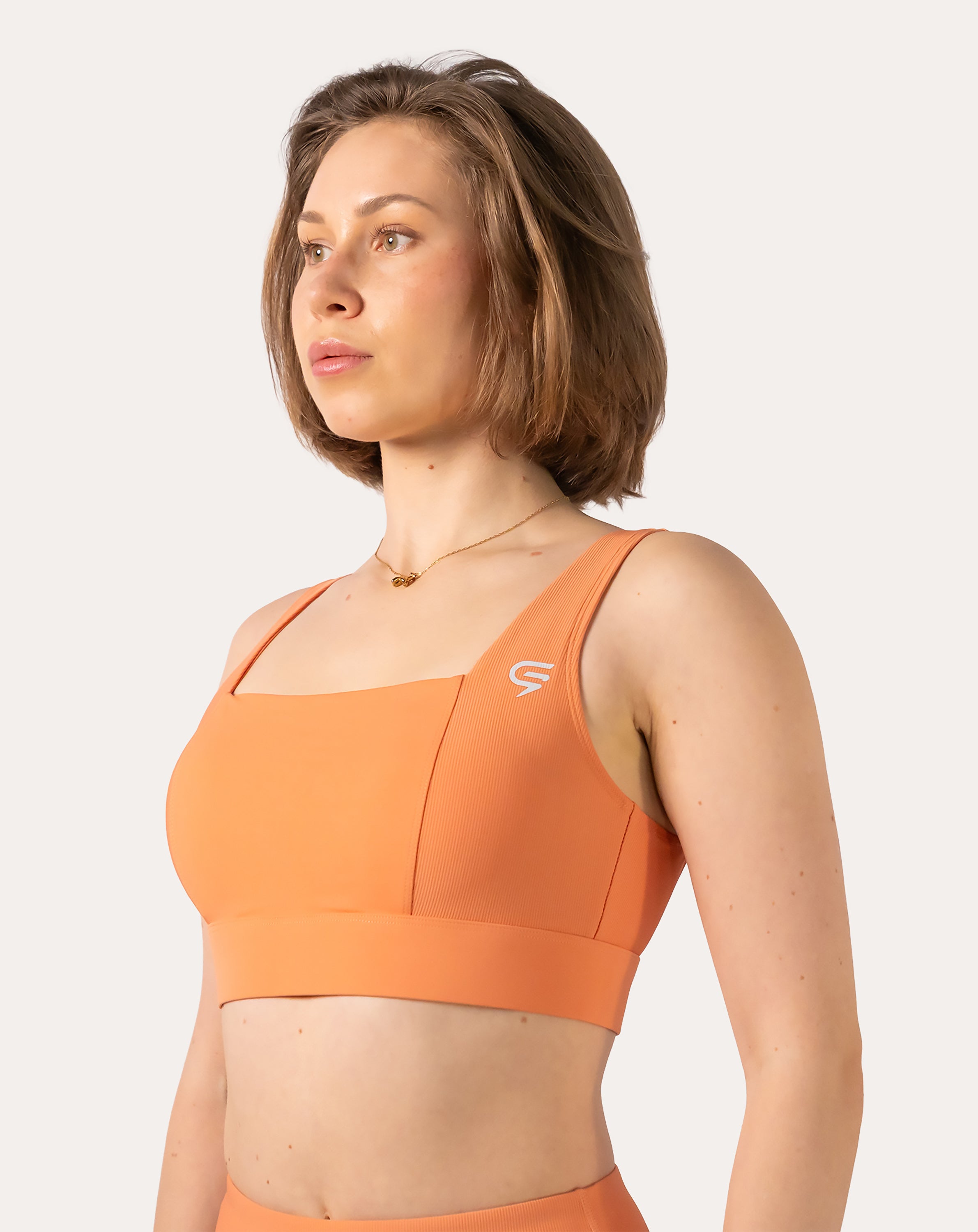 Front three-quarter view of orange sports bra with square neck and wide straps