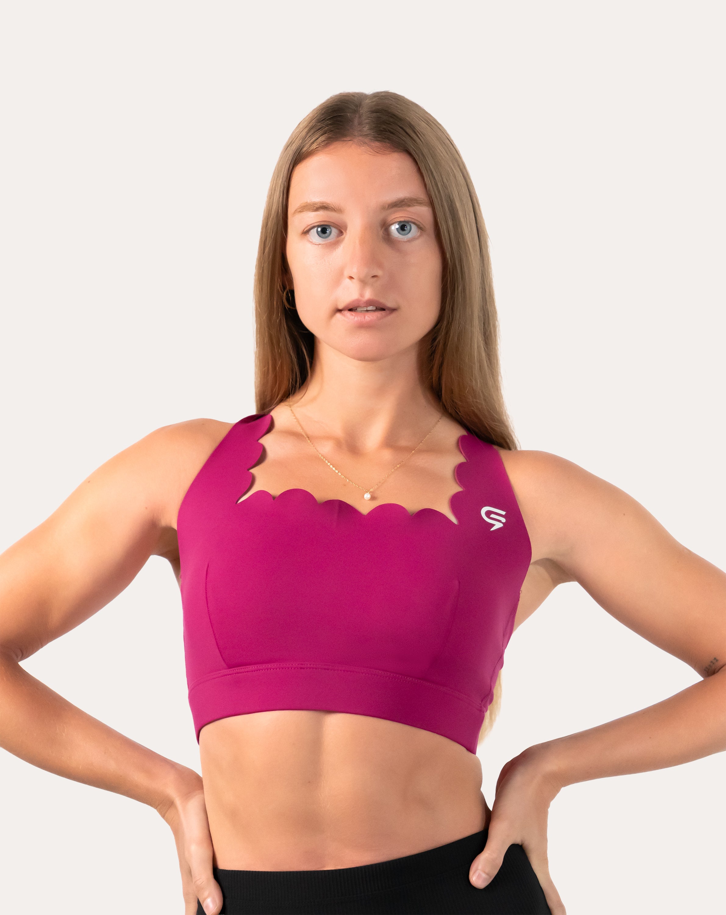 Front view of pink sports bra in magenta, scalloped neckline, hands on hips