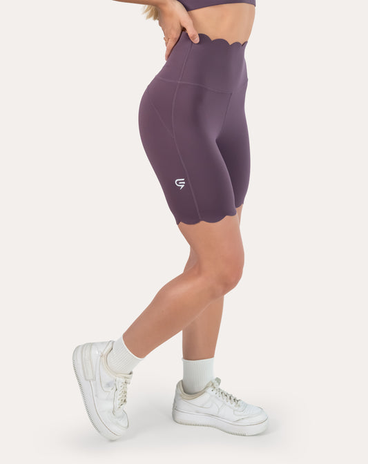 Left three-quarter close-up of plum gym shorts with scalloped high waist and hem