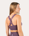 Left three-quarter back view of purple cross back sports bra highlighting crisscross straps