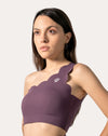 Front three-quarter view of purple sports bra with scalloped one-shoulder strap and wide underband