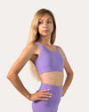 Purple sports bra in three-quarter front pose with hands on hips; smooth scoop neckline