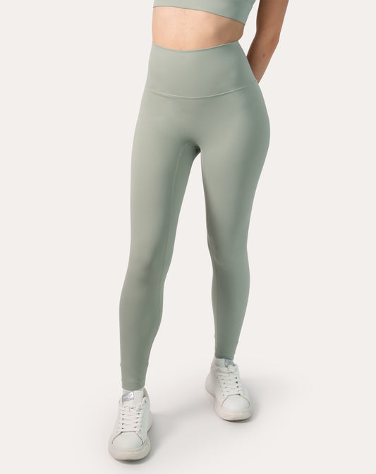 Front view of women’s seamless leggings in sage green with a wide high-waist band; smooth, ankle-length fit styled with white sneakers