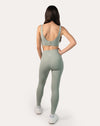 Three-quarter back view of matching set: seamless leggings and bra in sage green; secure high-waist and scoop-back top with white sneakers