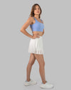 Full-body front three-quarter view of white pleated wrap gym skirt styled with sneakers