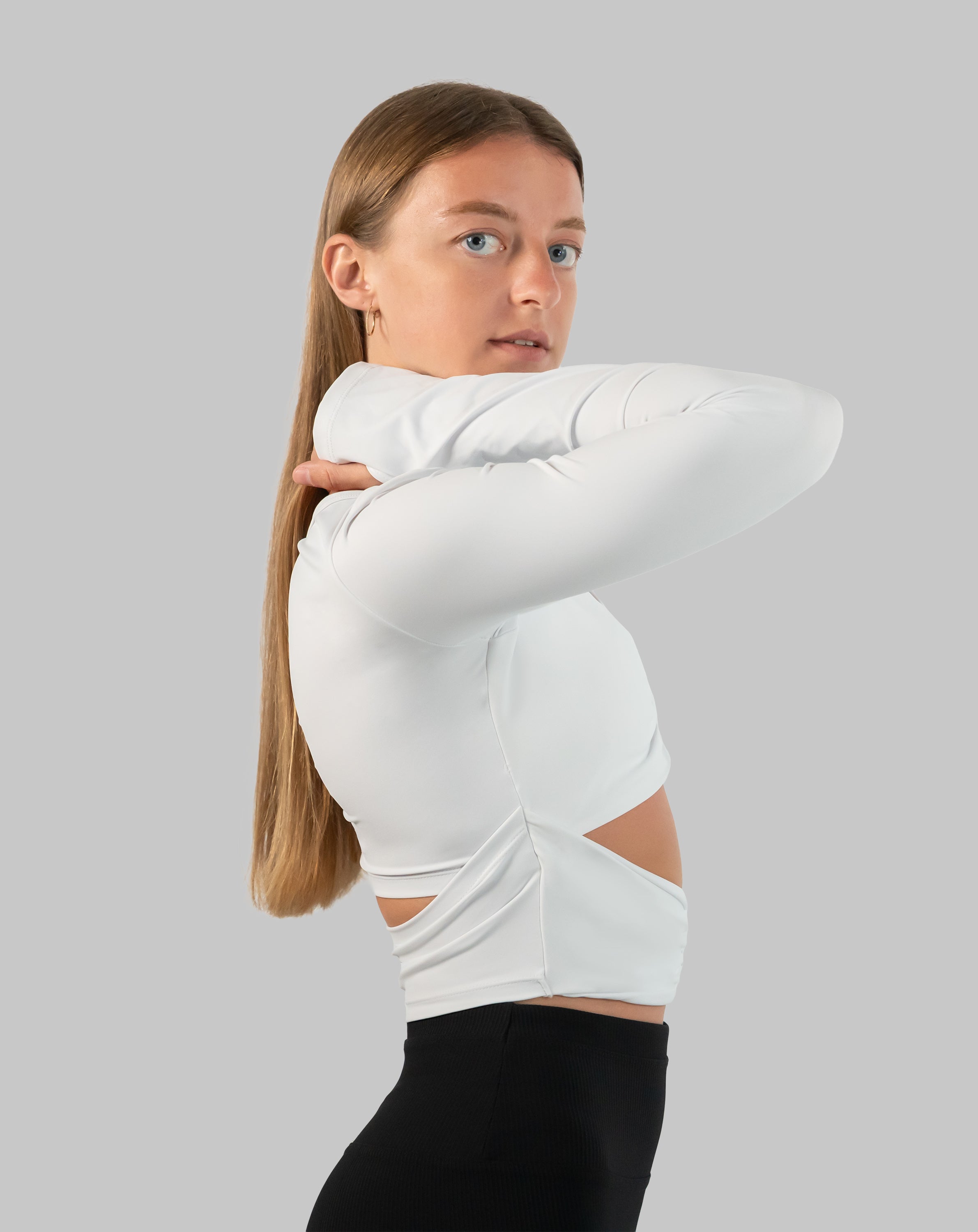 White gym top side profile showing long sleeves and cropped cut-out waist detail