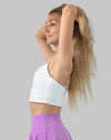 Front three-quarter view of the white medium support sports bra; scoop neck with right hand lifting hair