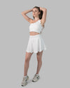 Women’s gym skirt set in white, model stretching in one-shoulder crop