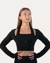 Front view of black long sleeve gym top womens with buckle and thumbholes, hands on hips