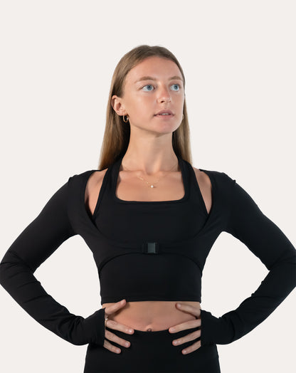 Front view of black long sleeve gym top womens with buckle and thumbholes, hands on hips